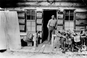 A man leaning against the doorframe of a log cabin.