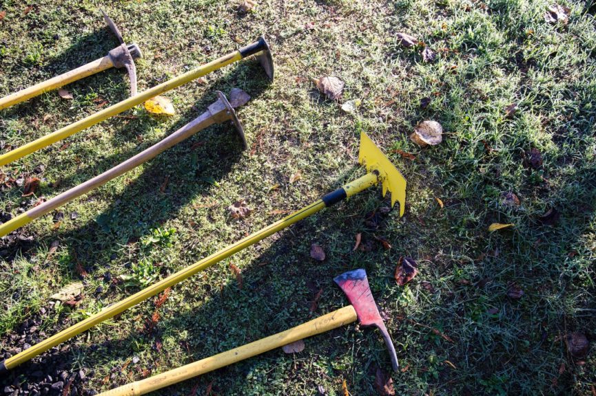Five long-handled trail tools laid out on a patch of grass.