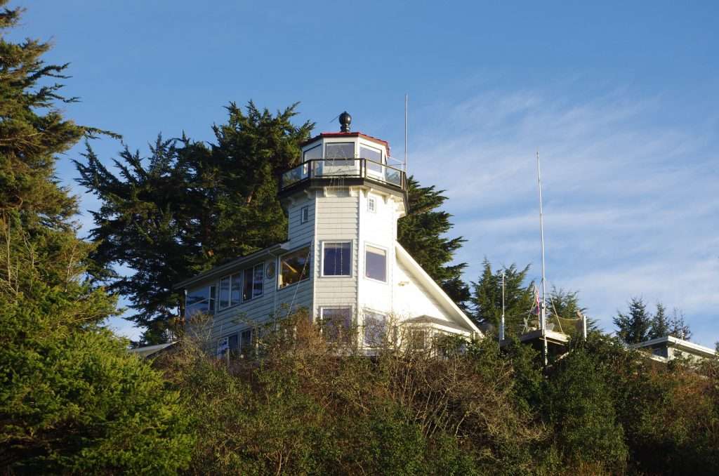 A lighthouse built into a residence with many windows and a large tree behind it.