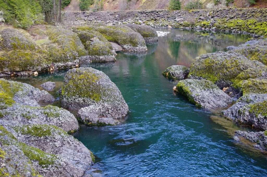 A clear blue river flows through an area of rounded boulders.