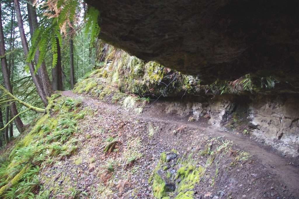A trail runs along a steep rock face under an overhang.
