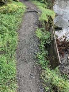 A board supporting the side of a gravel trail is falling away from the trail.