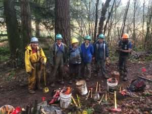 Six volunteers stand in front of a row of muddy trail tools smiling